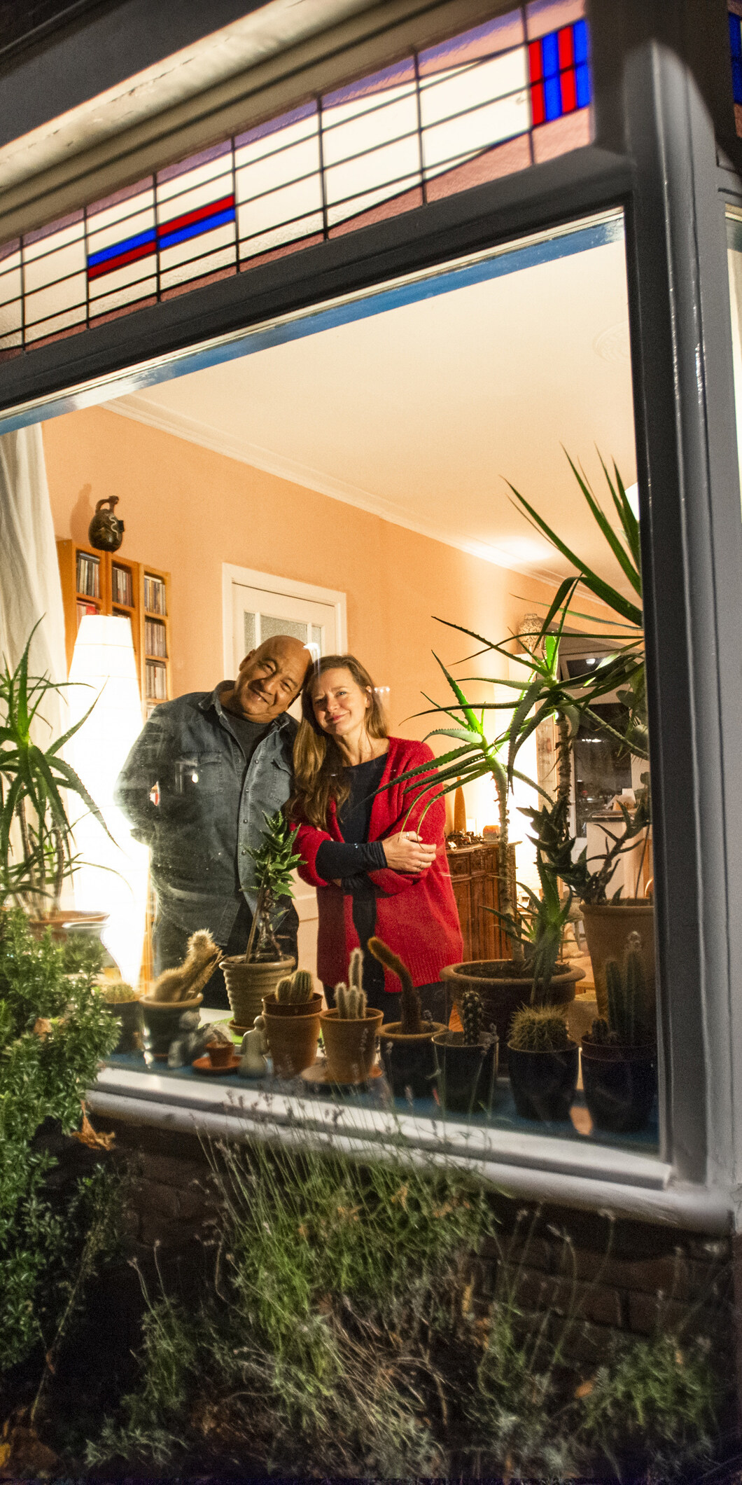 Een koppel staat samen achter hun raam, het is donker buiten en binnen brand warm licht