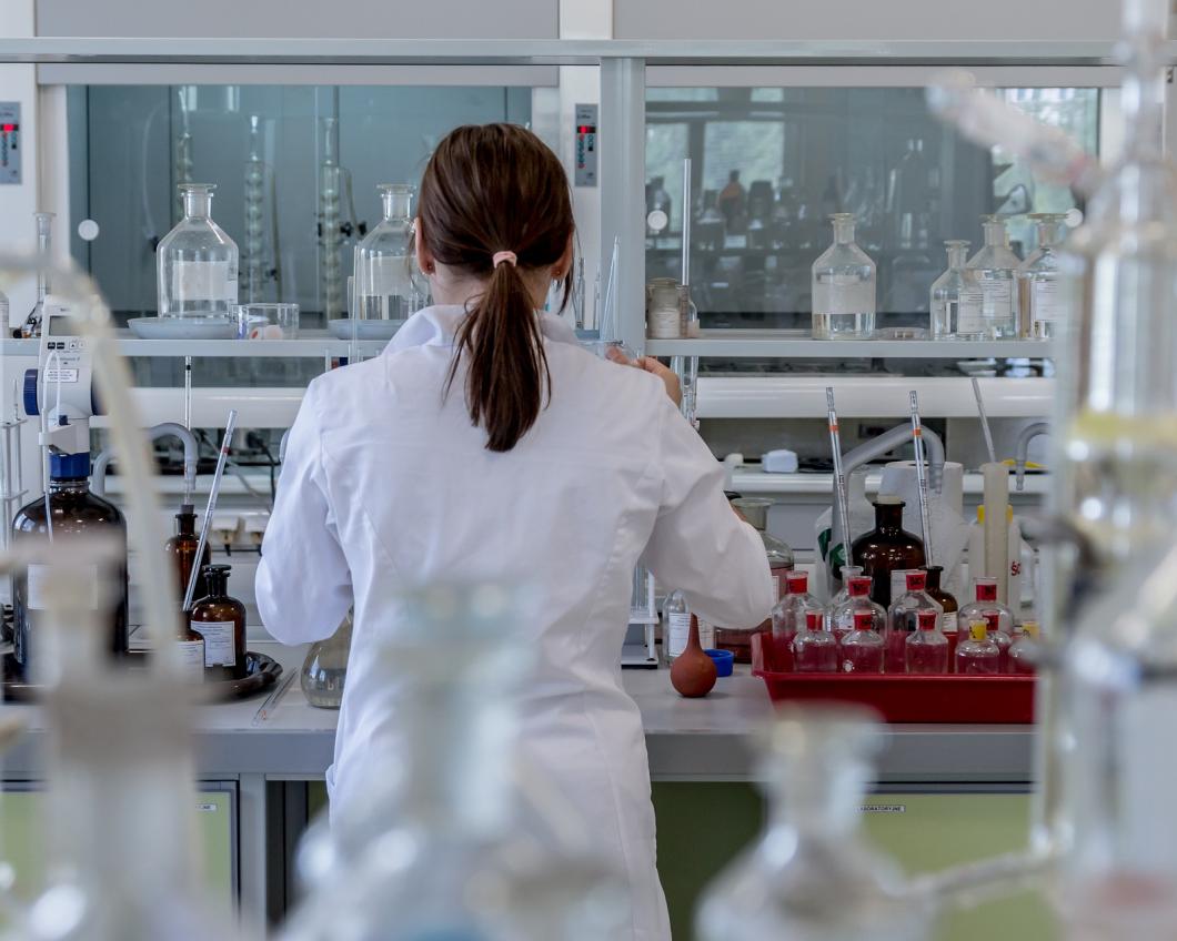 Een onderzoeker staat in een labratorium tussen de erlemeyers en ander onderzoeksmateriaal