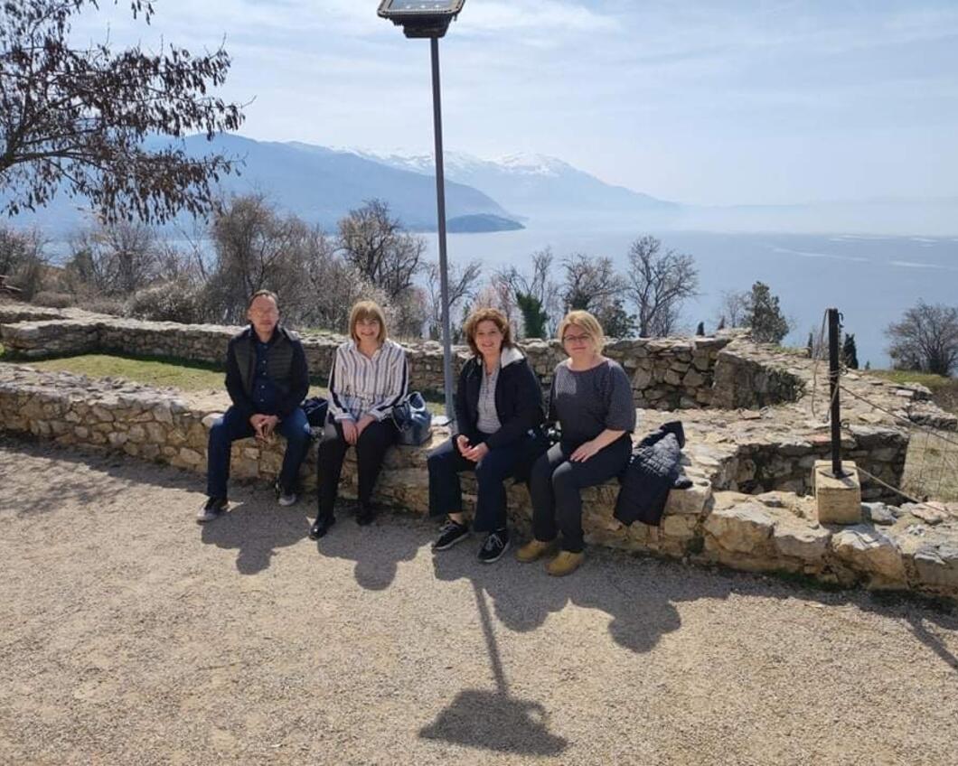 Group picture of 4 people including Gebke, sitting on the shore of lake Ohrid