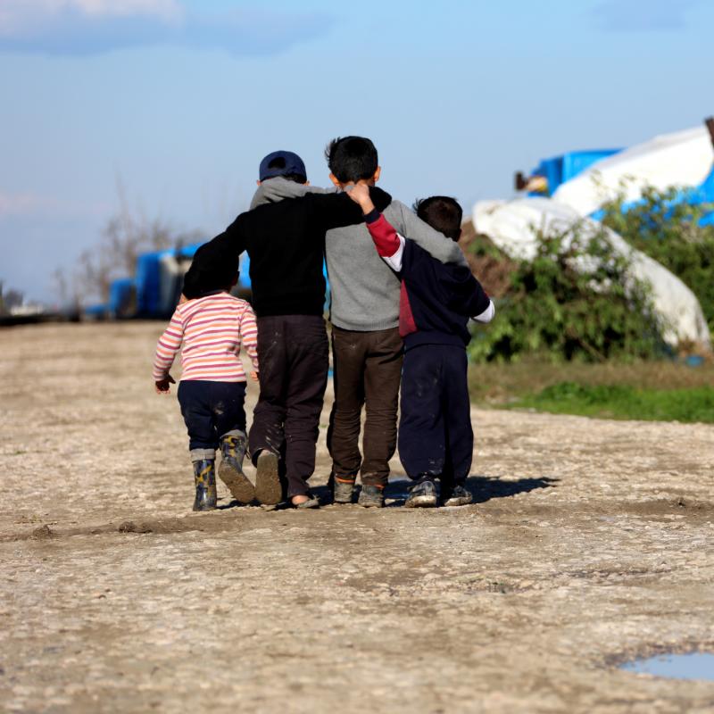 Vier kinderen lopen elkaar omhelzend, weg van de camera, over een zandweg