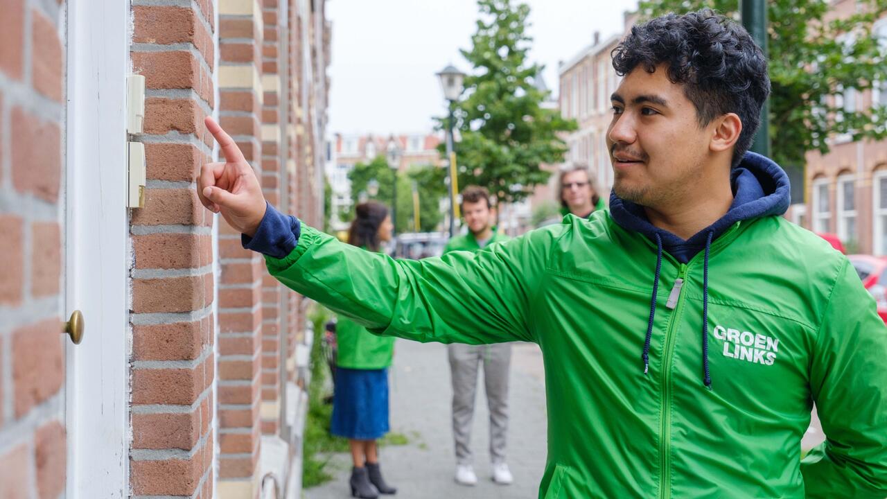 Een campagnevrijwilliger belt in een GroenLinksjasje aan bij een huis.